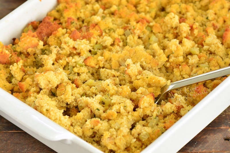 spooning cornbread dressing in a baking pan with a spoon scooping some out 