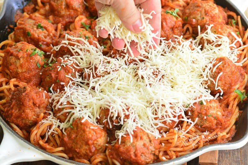 spreading cheese over meatballs in a pan with cheese on top 