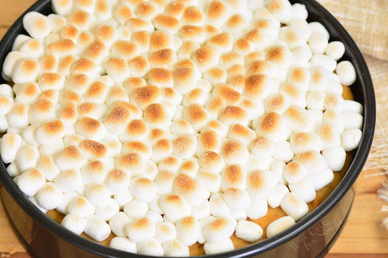 toasted marshmallows on the cheesecake that is sitting on a wood cutting board. 