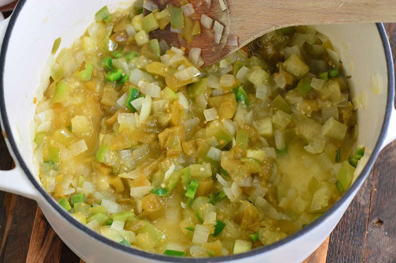 cooking vegetables and chopped chiles in a pot on a wood cutting board