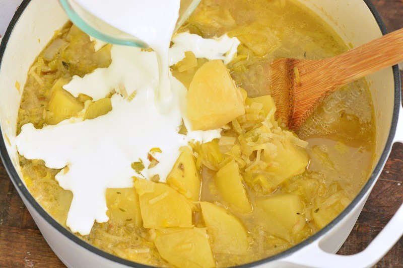 adding cream to cooked soup that is in a pot with a wooden spoon 