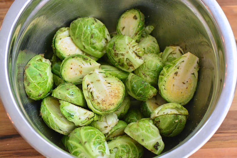 brussels sprouts tossed with oil and seasoning in a metal bowl 