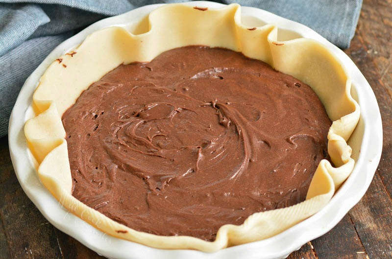 uncooked brownie batter in pie crust on a wood table with a blue towel 