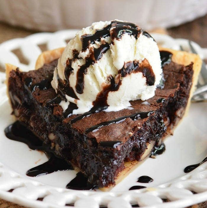 brownie pie slice with vanilla ice cream and chocolate sauce on top on a white plate 