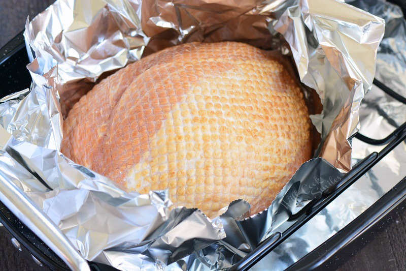 uncooked ham in foil in roasting pan.