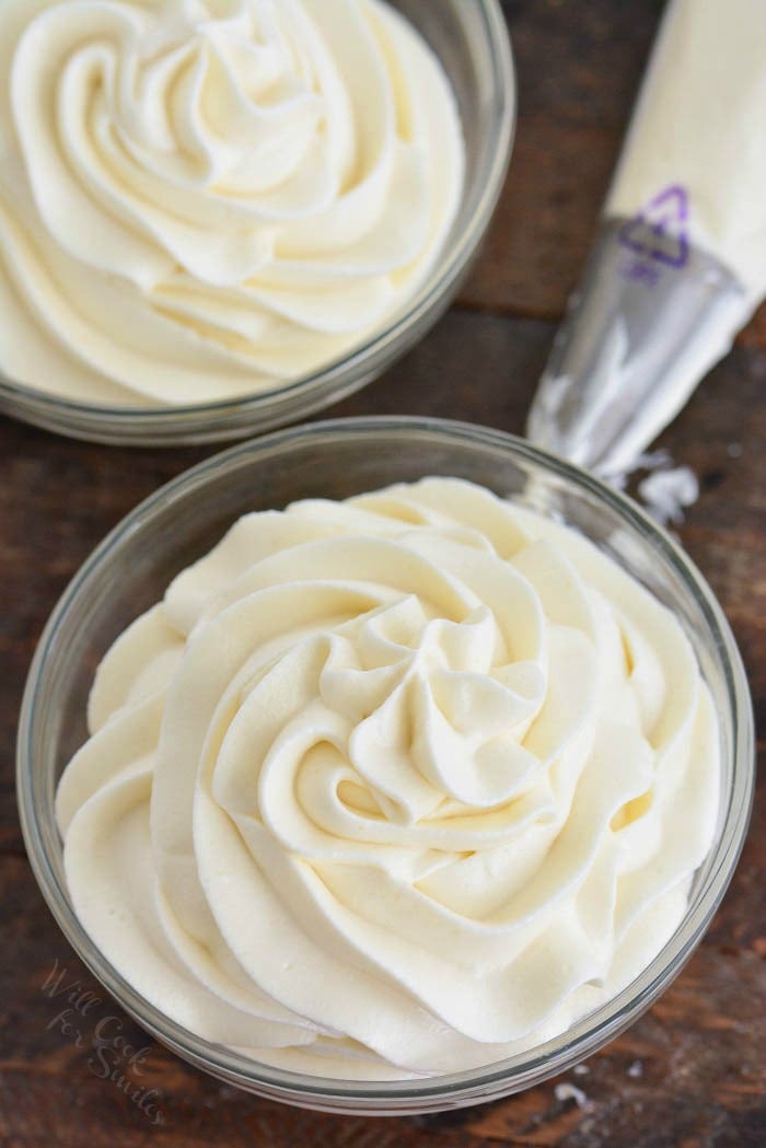 two Cream cheese frosting in a glass bowl, on a wood board 