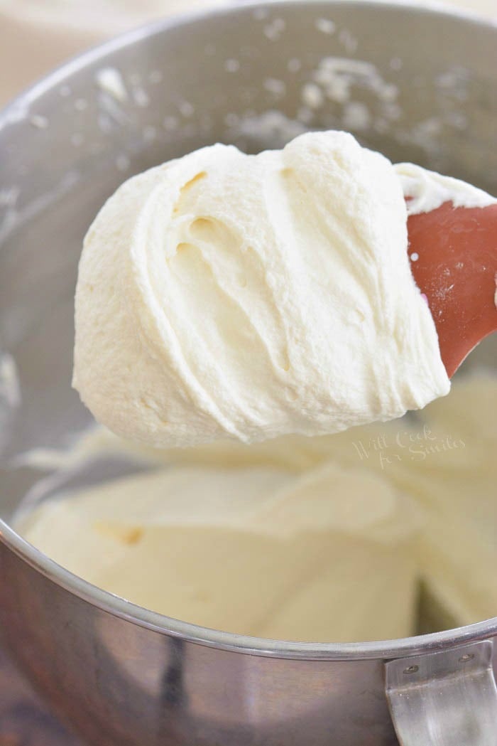 scooping cream cheese frosting out of a metal bowl with a spoon