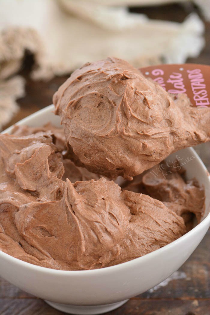 scooping chocolate cream cheese frosting out of a bowl