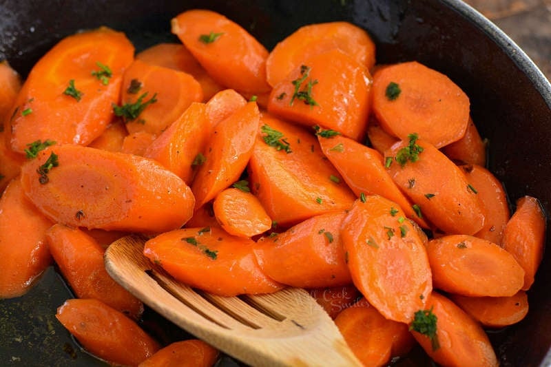 honey glazed carrots in a pan with a wooden spoon 