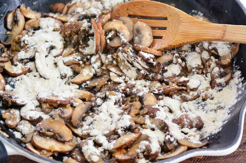 adding flour to pan of mushrooms, and stirring with a wooden spoon 