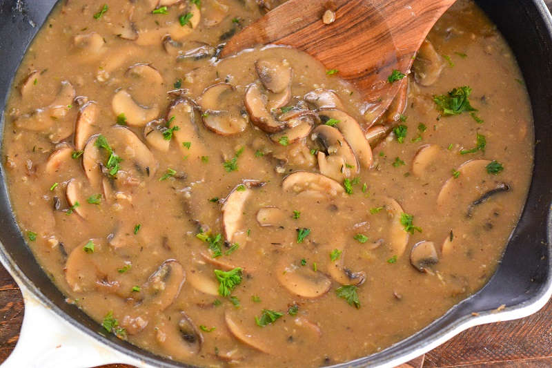 mushroom gravy in a cast iron skillet with a wooden spoon 