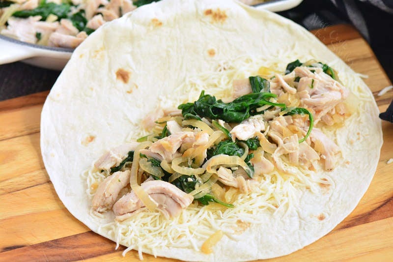 tortilla with turkey and spinach filling spread inside before rolling enchiladas.