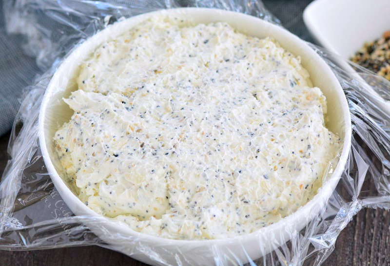 cream cheese mixture in a bowl with plastic wrap on a wood cutting board 