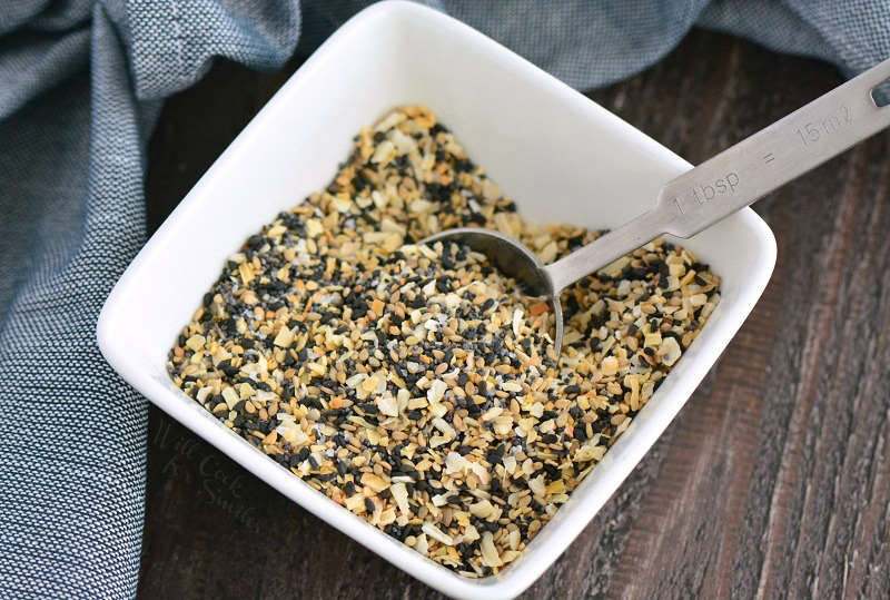 everything bagel seasoning in small bowl with a tbsp on wood board 
