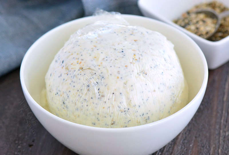 shaped cheese ball in plastic wrap in a bowl on a wood cutting board 