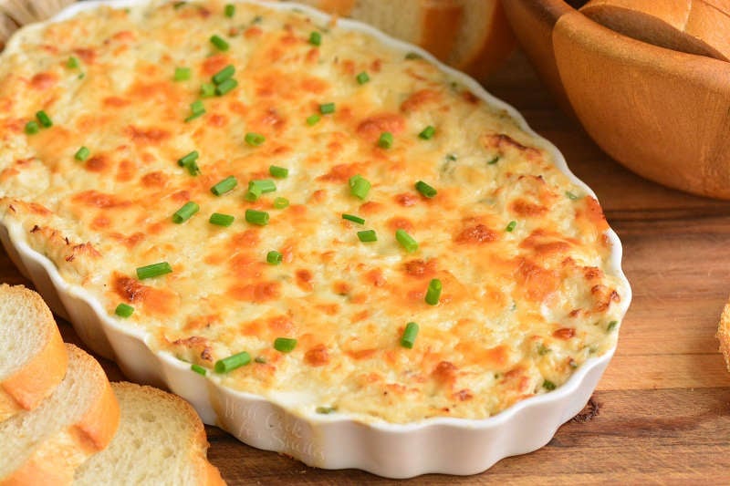 baked crab dip in a glass serving bowl on a wood cutting board 