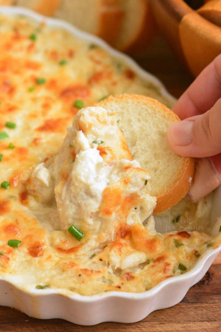scooping some hot crab dip with a slice of baguette
