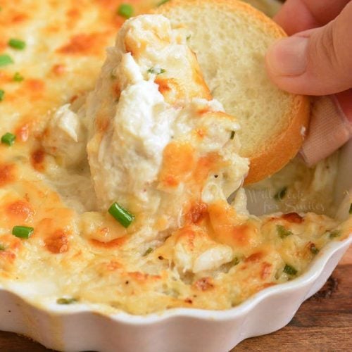 crusty bread being dipped into crab dip in a baking dish