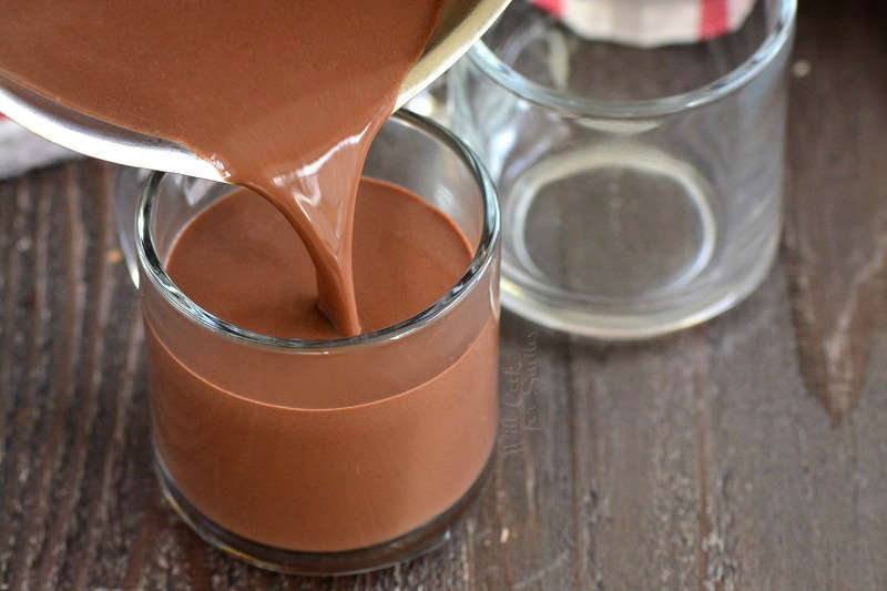 pouring hot chocolate into glasses that are on a wood cutting board 