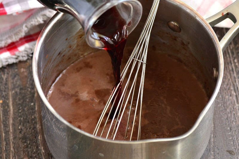 pouring wine into hot chocolate mixture that is in a pan with a wire whisk 