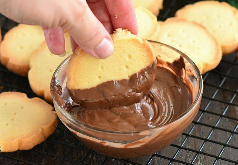 dipping cookie into chocolate in a glass bowl on a cooling rack 