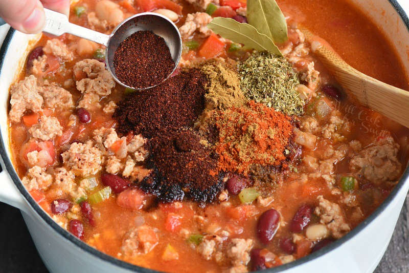 adding spices to chili in a pot 