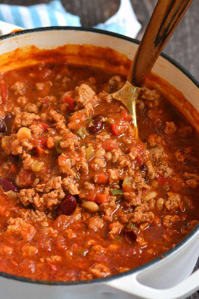 pulling out a ladleful of turkey chili in a white pot 