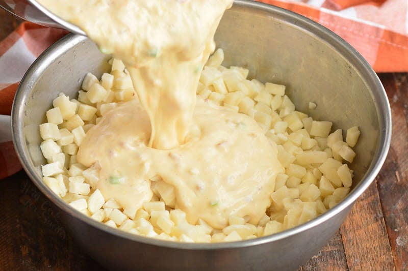 pouring cheese sauce into potatoes that is a metal bowl 