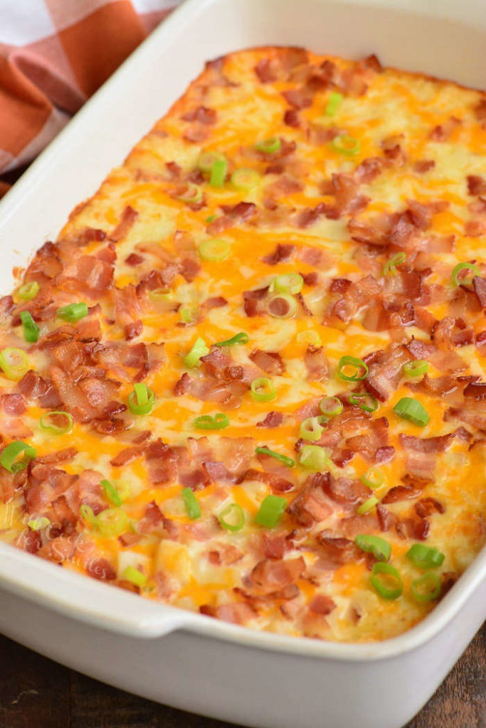 baked potato casserole in a white dish topped with bacon and green onions.