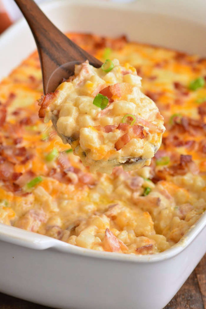 pulling out a spoonful of cheesy potatoes out of the white casserole dish.