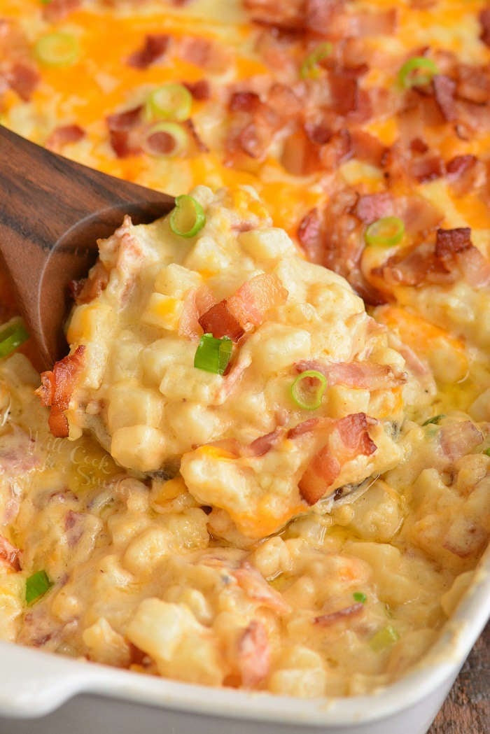 close-up of scooping cheesy potato casserole with wooden spoon.