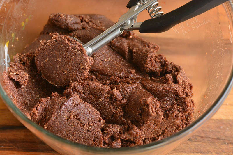 rum ball dough in a glass bowl being scooped out with cookie scoop 