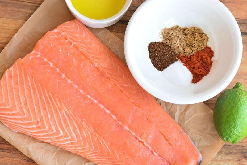 ingredients for baked salmon on parchment paper on a wood cutting board with seasoning 
