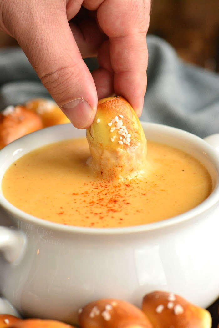 Beer cheese dip in a bowl surrounded by pretzel bites and dipping a pretzel bite in the cheese 