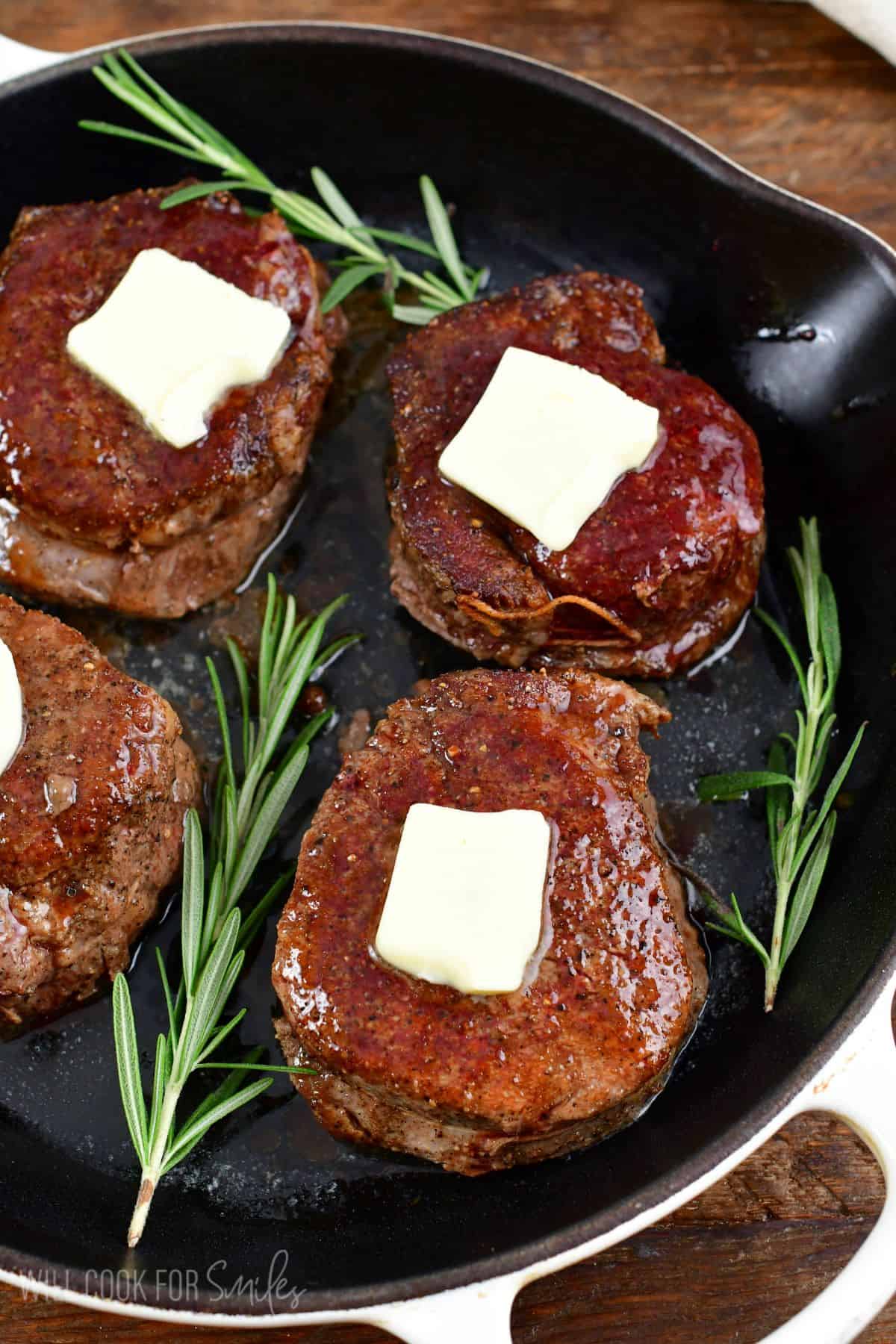 four filet mignon steaks in the skillet with butter and rosemary sprigs.