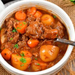 a light bowl filled with beef stew and vegetables and a silver spoon.
