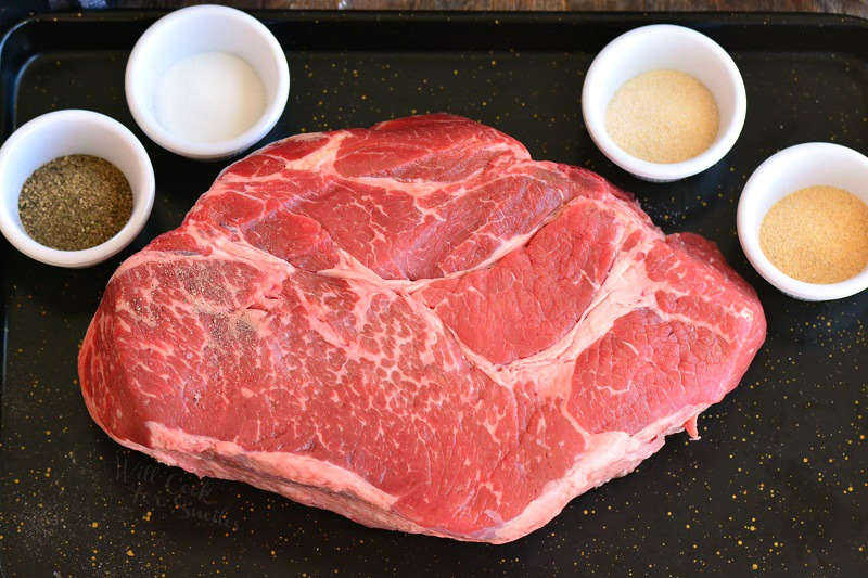 beef chuck roast with seasoning on a baking sheet 