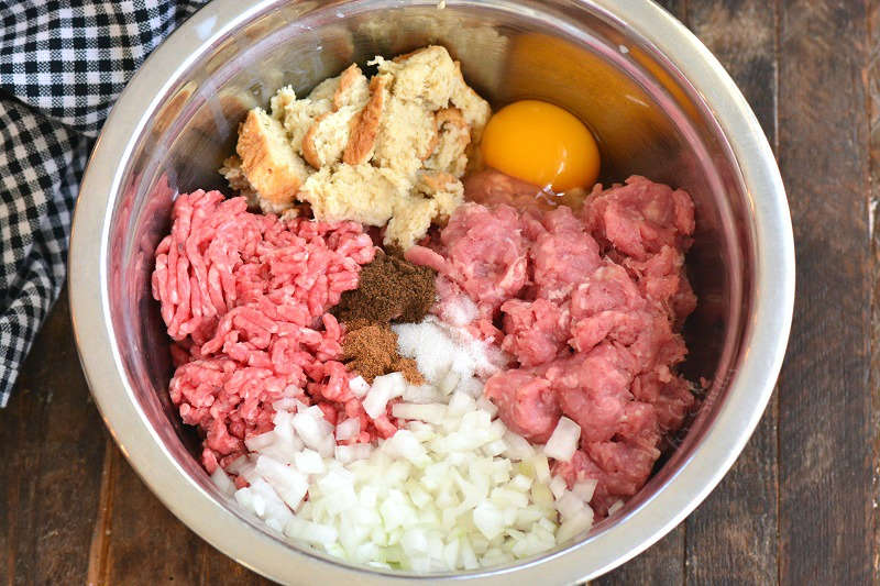 ingredients for the meatball mixture in a metal bowl on wood cutting board 