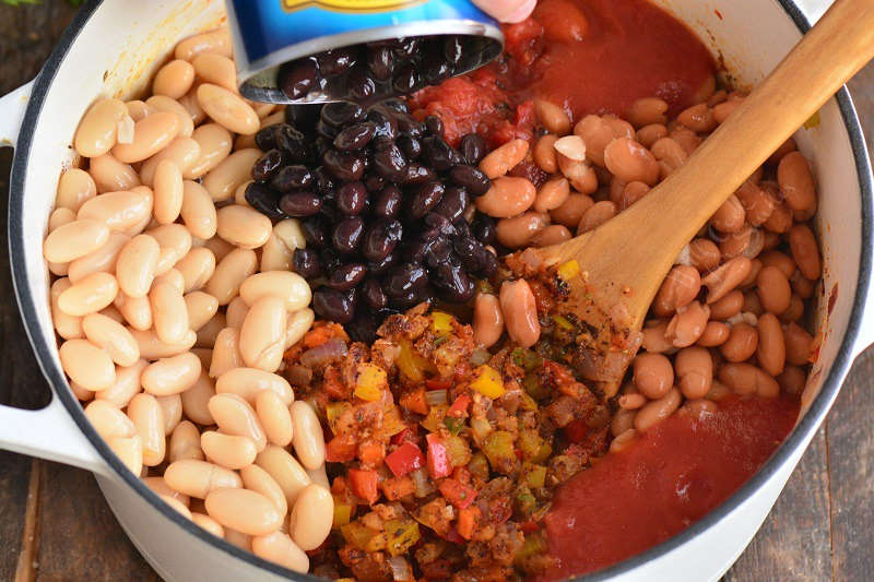 adding beans to the pot with veggies for chili. 