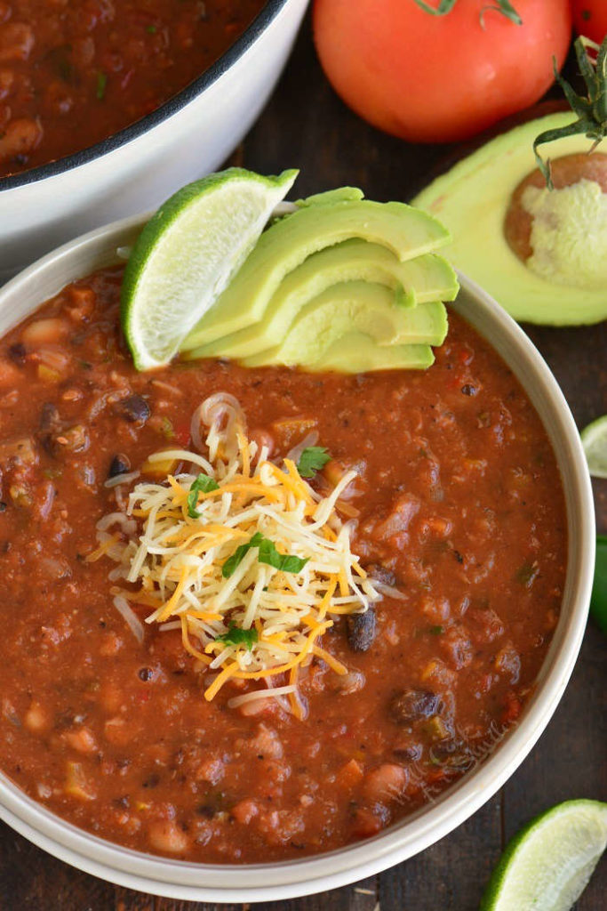 top view of vegetable chili in a bowl with cheese and avocado.