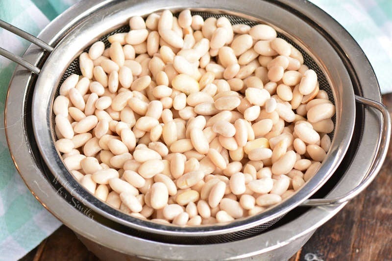 soaked beans in a strainer and metal bowl on a wood table 