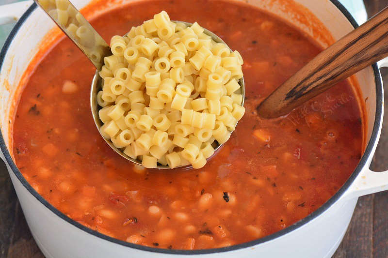 adding pasta to the soup that is in a pot 