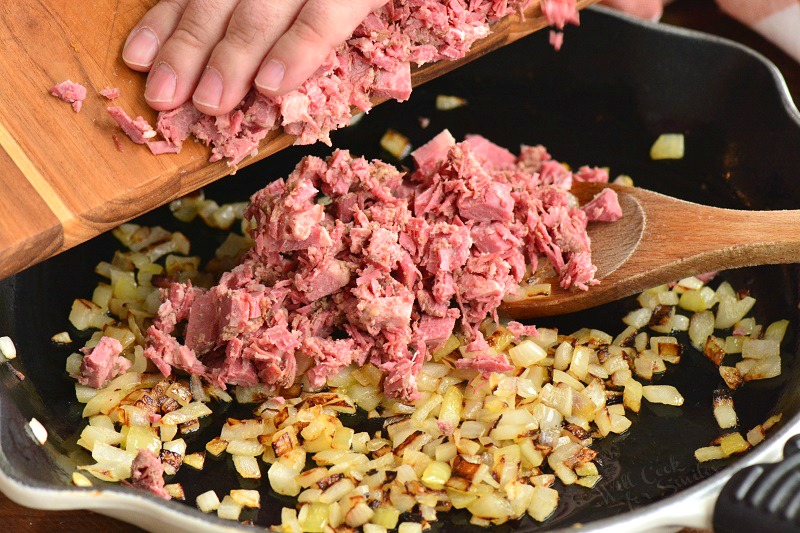 adding diced corned beef to the onions in a skillet.