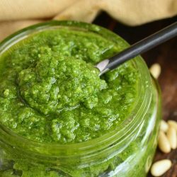 closeup of spooning out some pesto from glass jar.