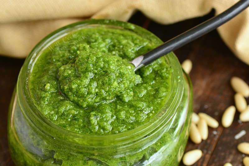 closeup of spooning out some pesto from glass jar.