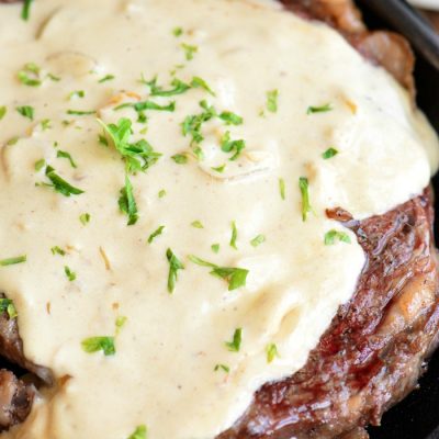 closeup of ribeye steak covered in a cream sauce and parsley.