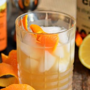a rocks glass filled with whiskey sour cocktail and an orange twist, more twists around.