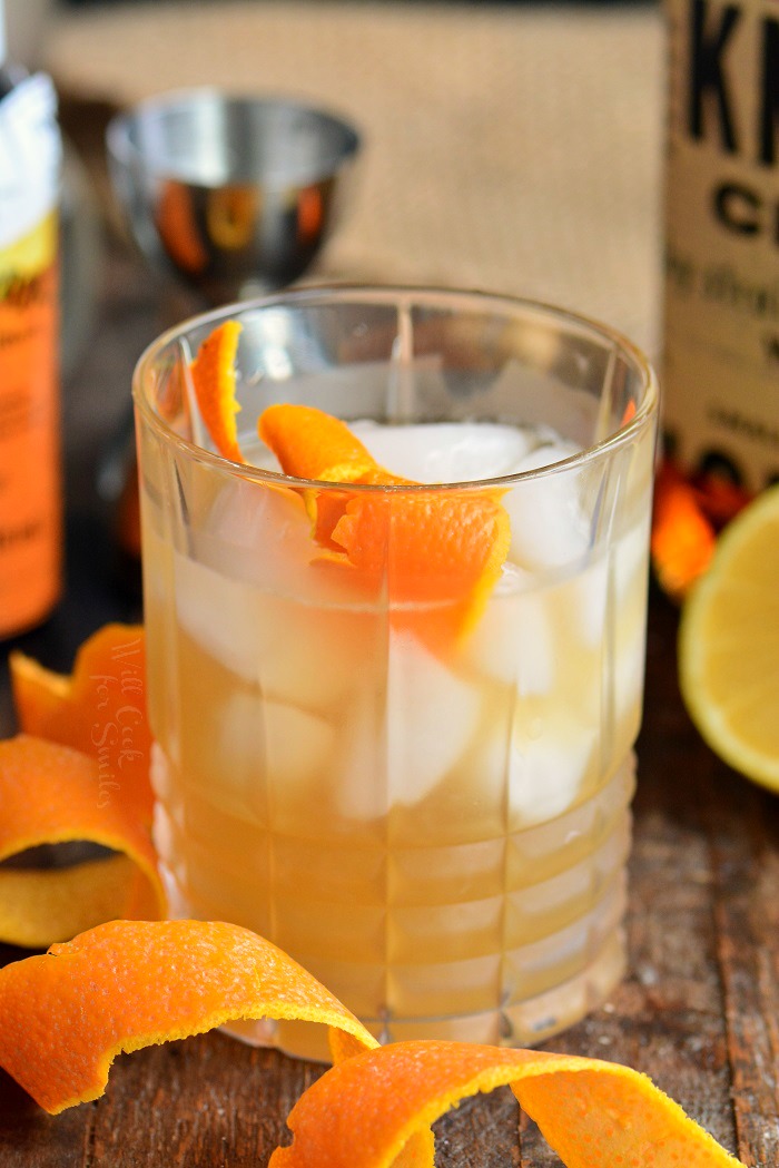 a rocks glass filled with whiskey sour cocktail and an orange twist, more twists around.