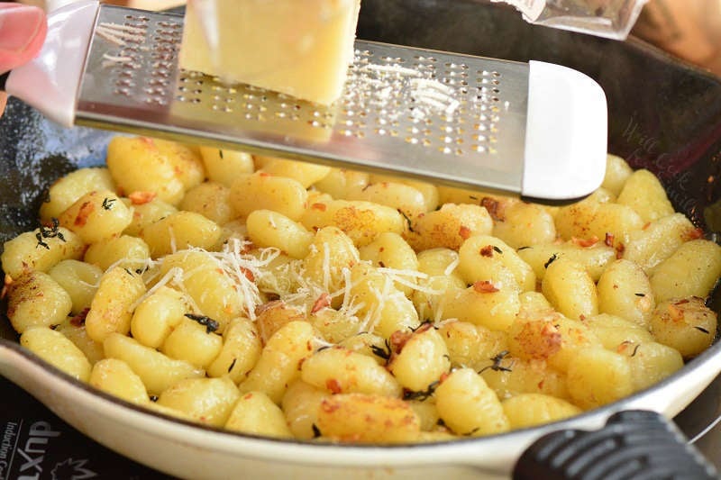 grating Parmesan cheese to the pan with potato gnocchi