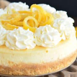 whole lemon cheesecake topped with frosting rosettes and lemon peels.